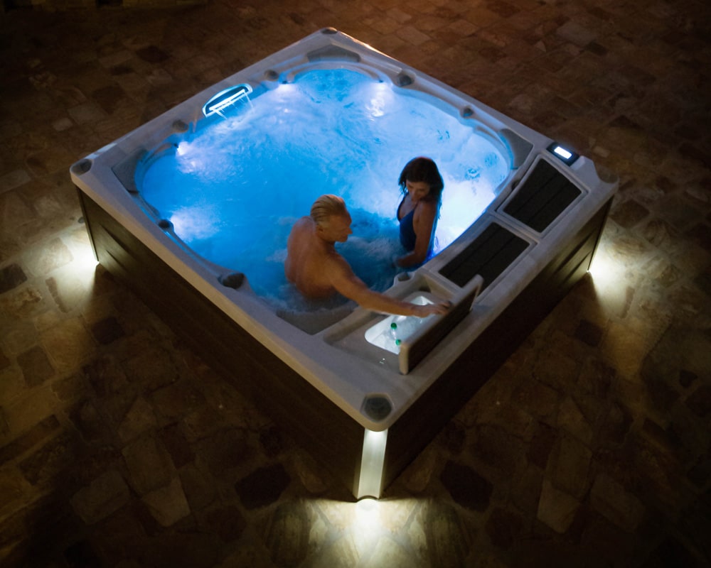 couple in a hot tub at night. man is opening storage with refreshments